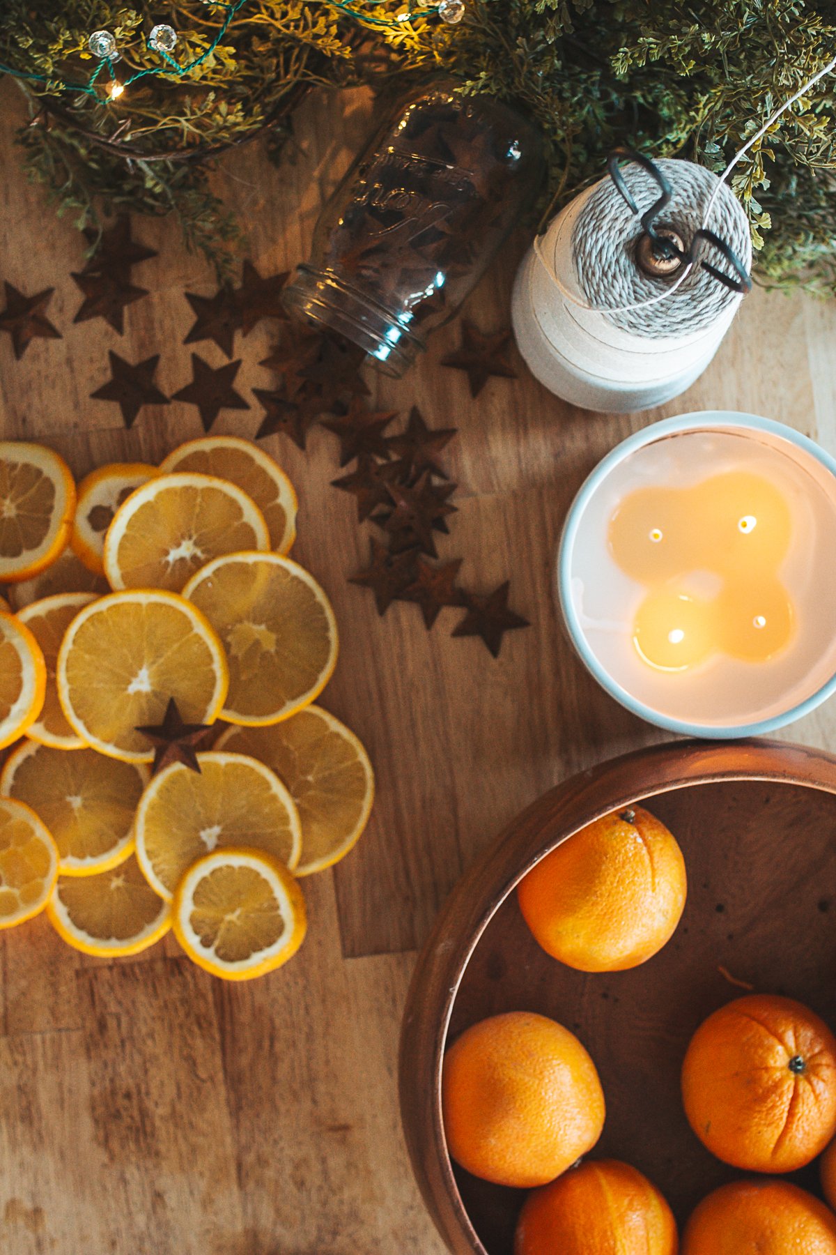 fresh sliced oranges and whole oranges waiting to be sliced on counter beside candle and string.