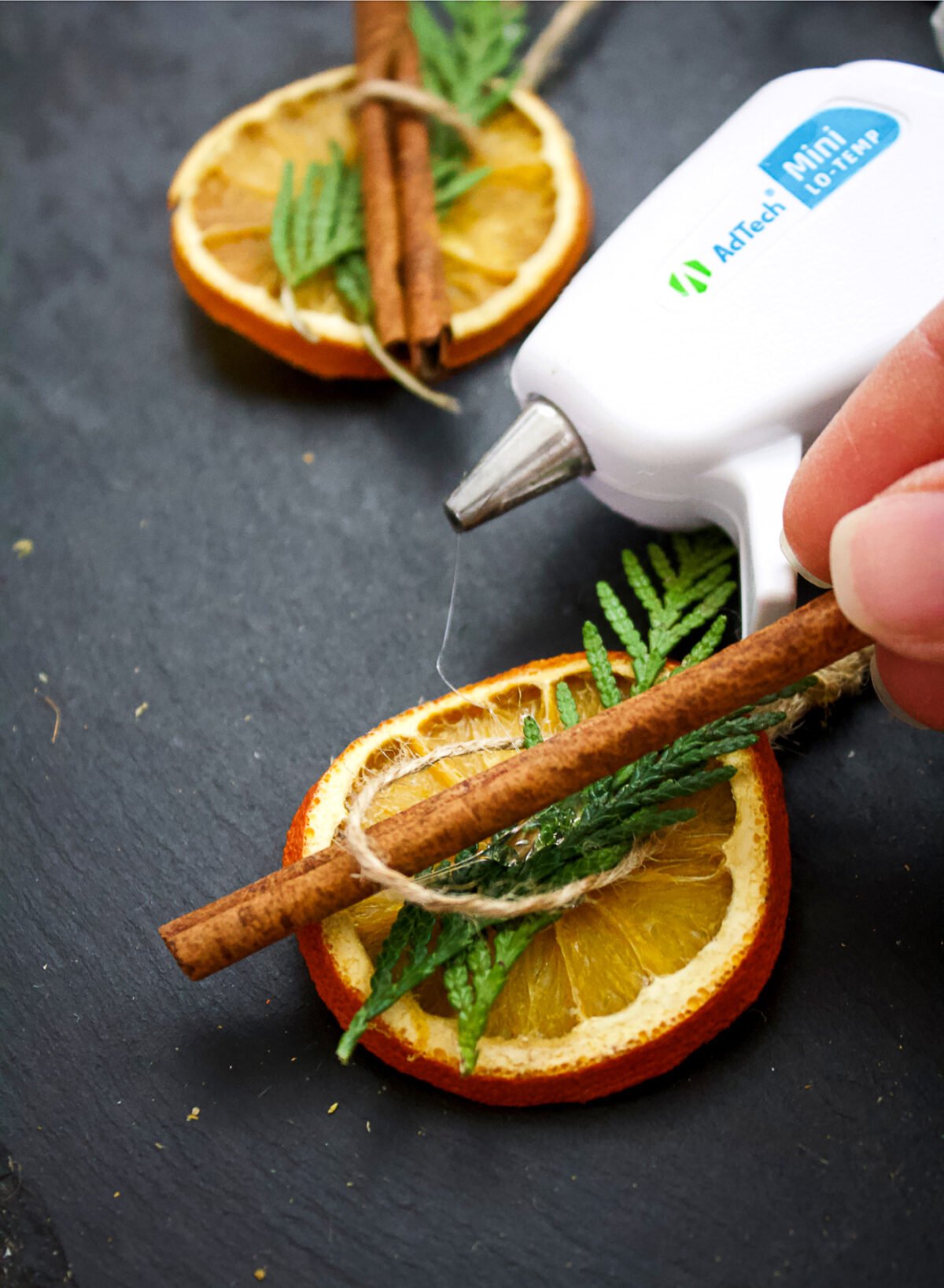 orange being hot glued to a cedar bough and cinnamon stick to make an ornament.