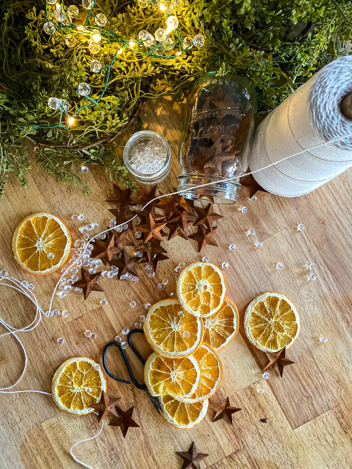 Dried orange slices next to tin stars, string, and crystals to assemble a garland.