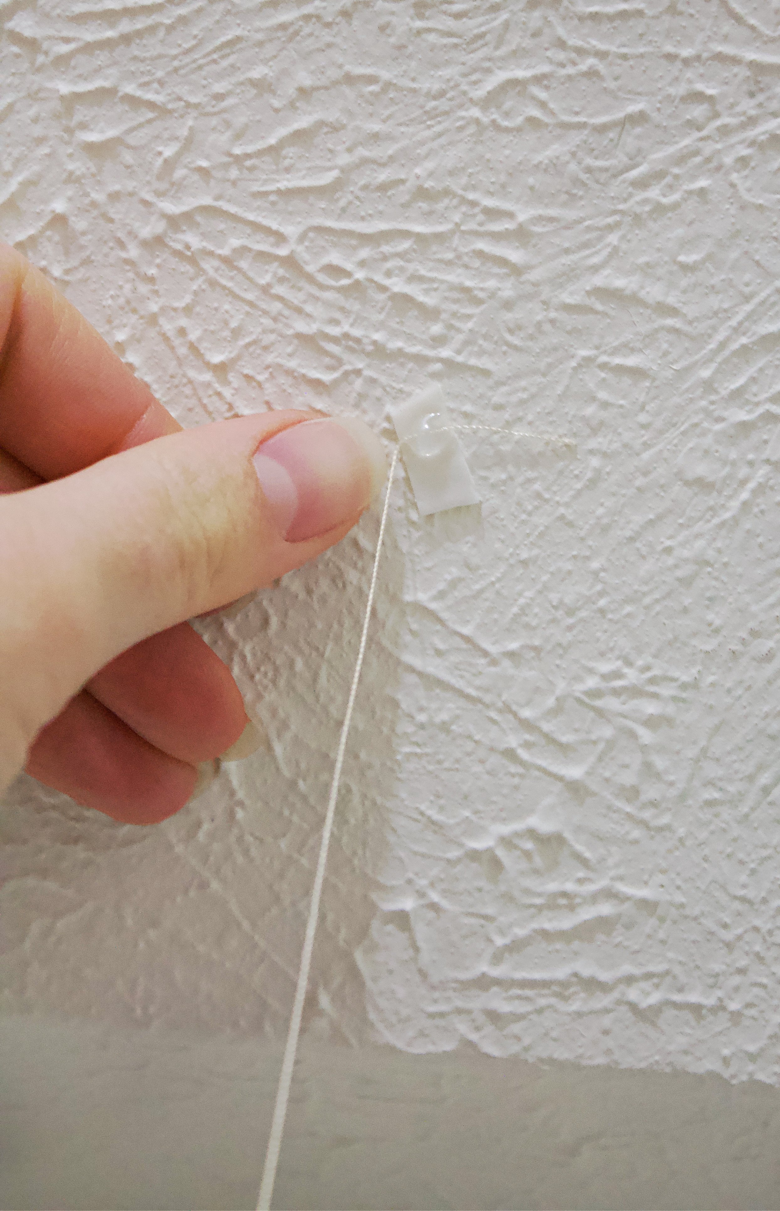Showing a hand attaching the garland to the ceiling with a cut up command strip.
