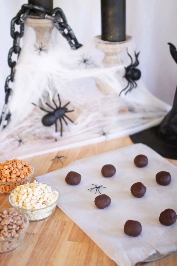 chocolate cookie dough rolled in 1" balls on parchment paper with Halloween decor all around.