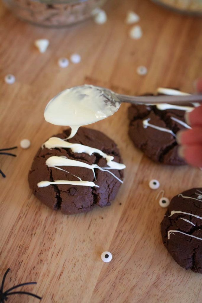 Drizzling white chocolate over a chocolate cookies on a wooden counter