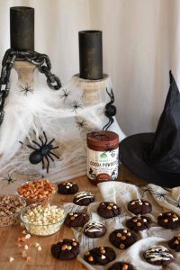 Chocolate cookies in a spooky Halloween backdrop with candles, webbing, spiders, and a witch hat.