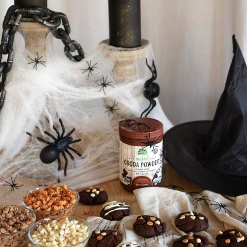 Chocolate cookies in a spooky Halloween backdrop with candles, webbing, spiders, and a witch hat.