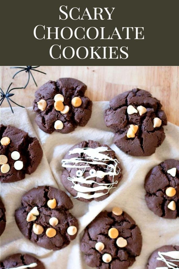Chocolate cookies with white chocolate drizzle and different candy chips sprinkled on top, set on a wooden counter with script on top that says scary chocolate cookies.