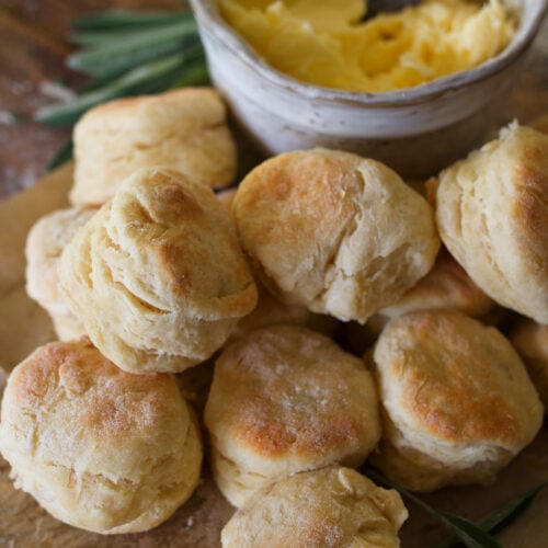 biscuits next to a bowl of butter on a wooden counter.