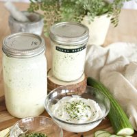 Jars of rach dressing with spices on wooden counter with cucumber slices.