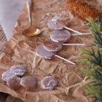 Honey suckers and lozenges on parchment paper with a spoon full of honey and a honeycomb on the side.