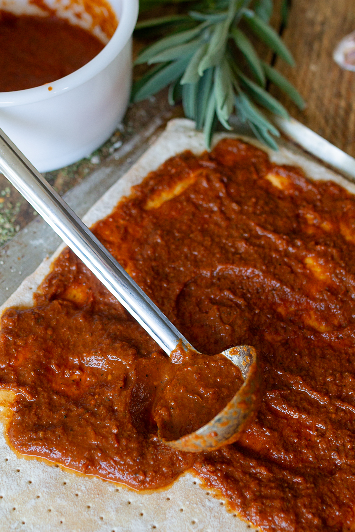 Stainless steel spoon placing pizza sauce onto crust.