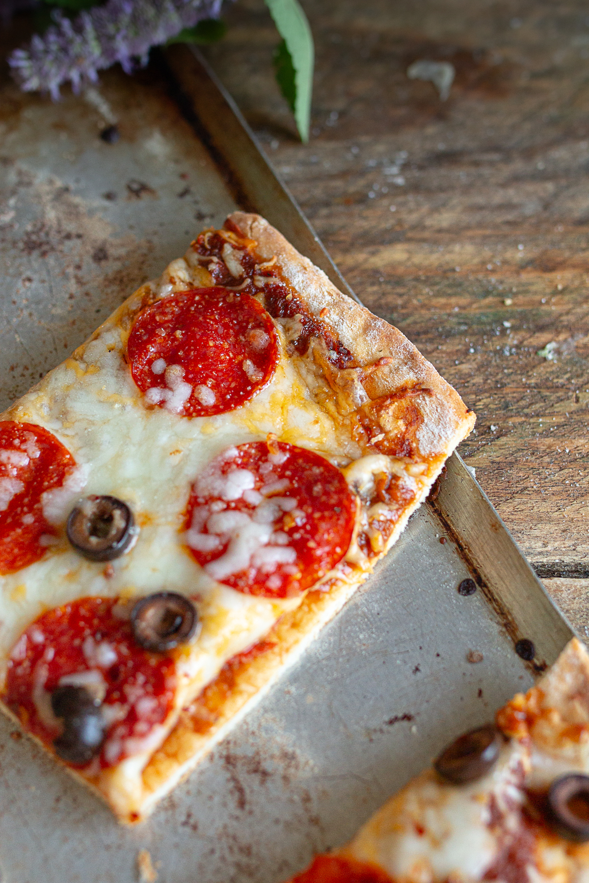 A close-up shot of a single square slice of homemade sheet pan pepperoni and black olive pizza on a vintage metal tray.