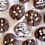 chocolate cookies on a wooden counter, some of the cookies have chocolate chips in them, some are drizzled in white chocolate to look like mummies.