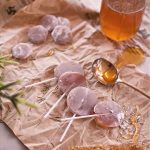 Honey suckers and lozenges on parchment paper with a jar of honey and spoon full of honey.