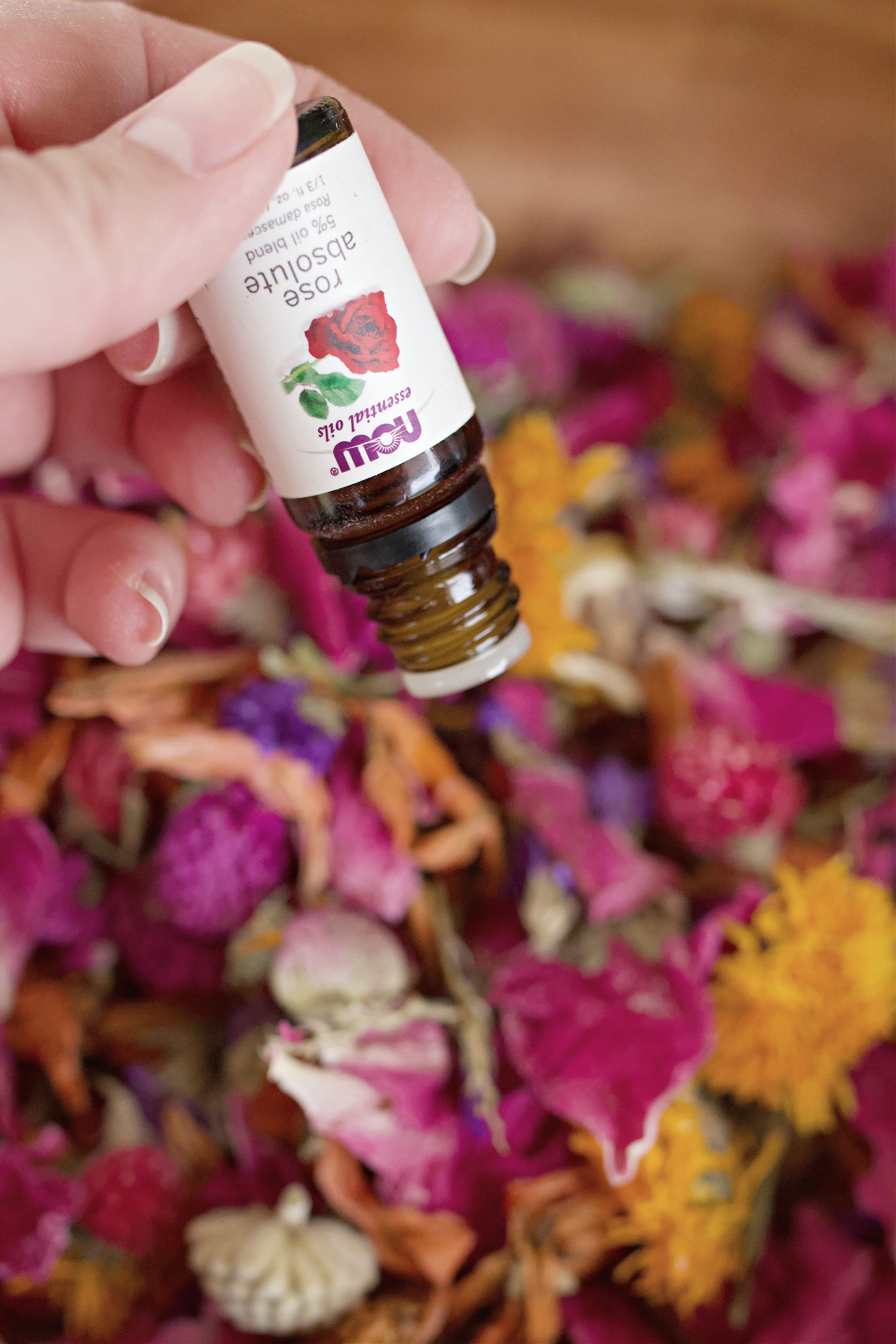 dropping rose essential oil into a wooden bowl of dried flowers. 