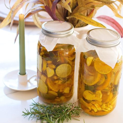 two half gallons of fire cider on a counter next to a plant and candle