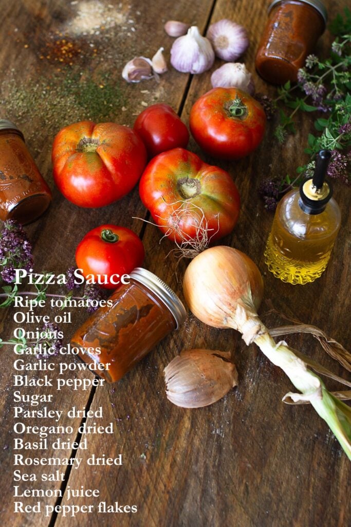 Fresh garden tomatoes, garlic bulbs, whole onions, and a bottle of olive oil arranged on a rustic wooden table with an overlay list of home-canned pizza sauce ingredients.