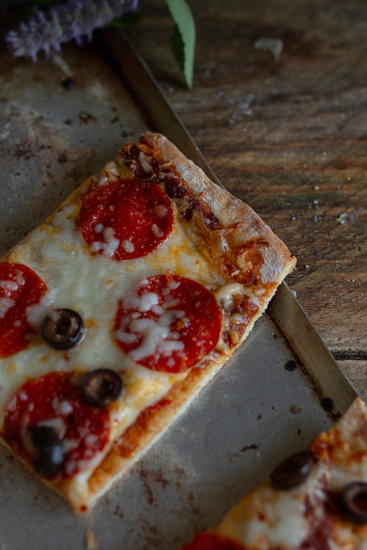 Piece of pizza on stainless steel pan on wooden counter. 