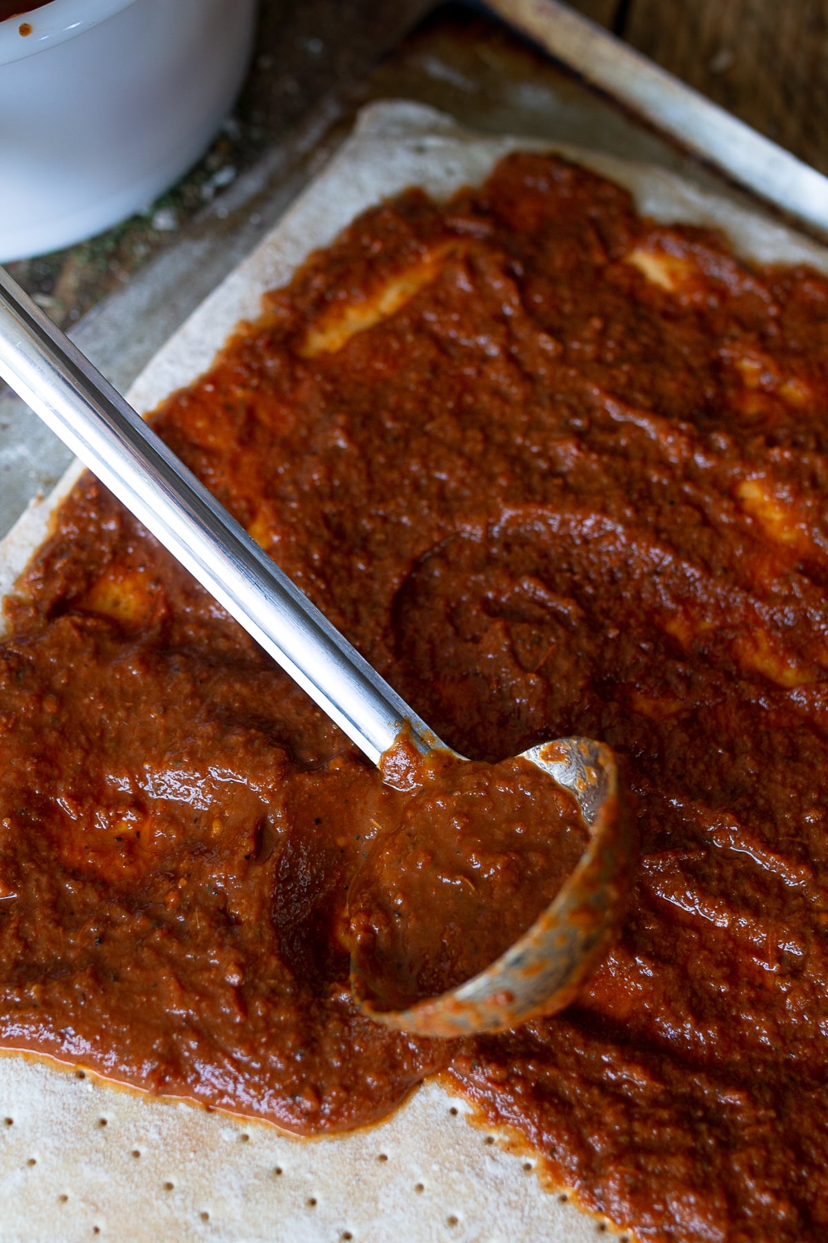 Stainless steel spoon placing pizza sauce onto crust. 