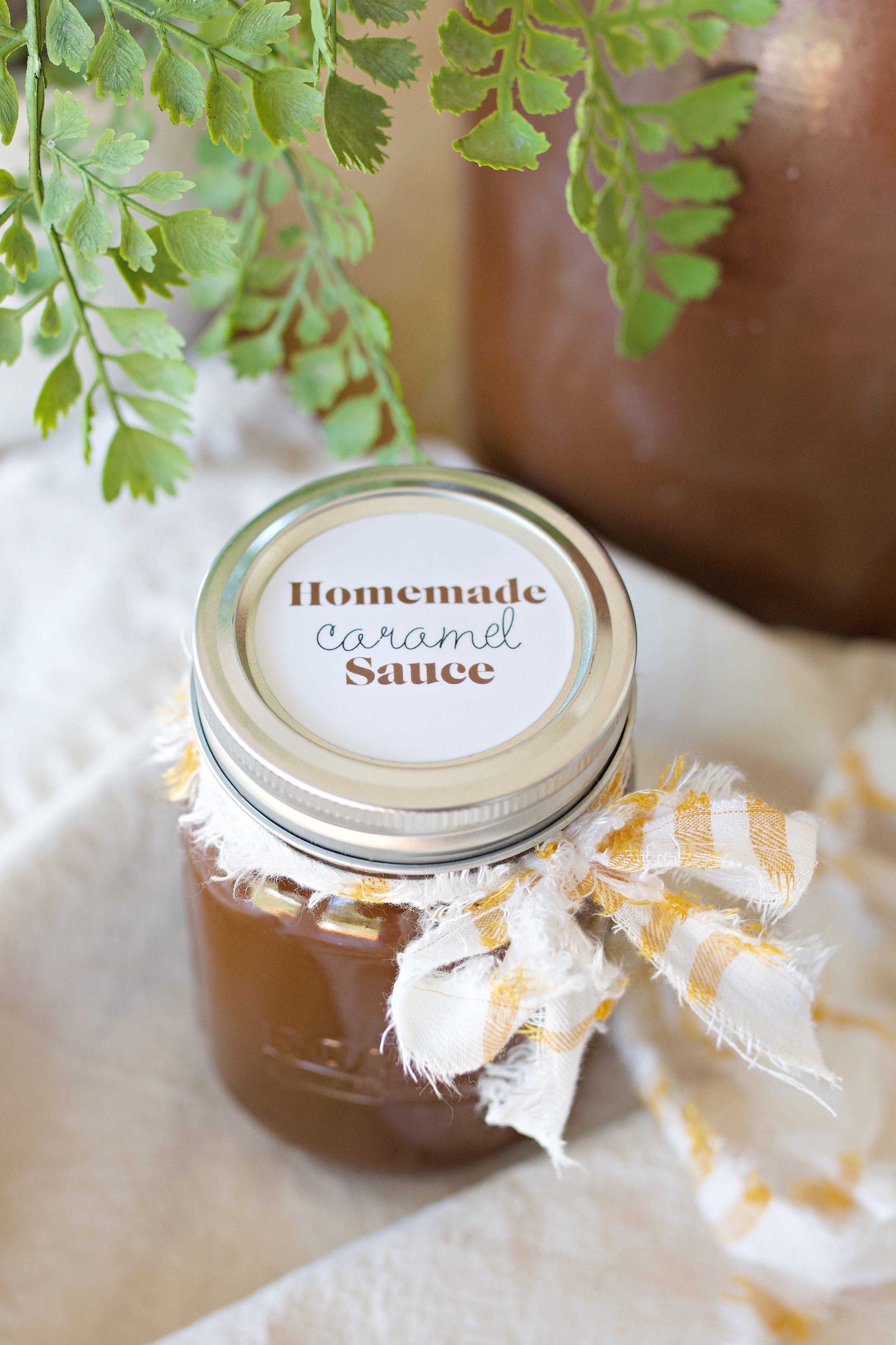 Jar of homemade caramel sauce on counter decorated with a fabric tie ready for gifting.
