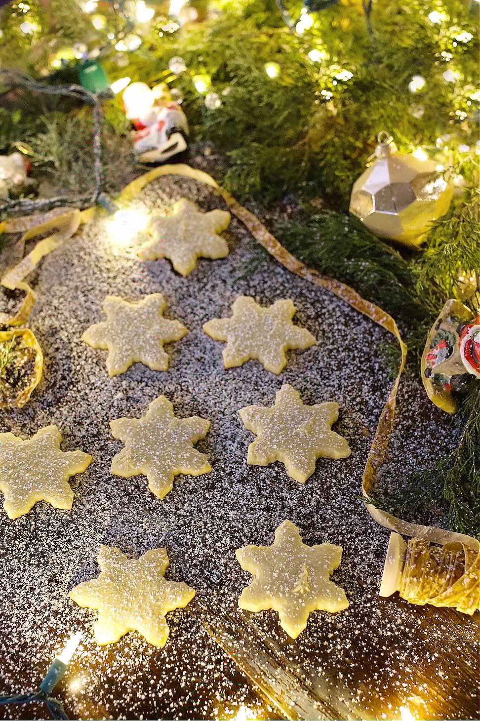 Sugar cookies on counter surrounded by greenery dusted with powdered sugar.