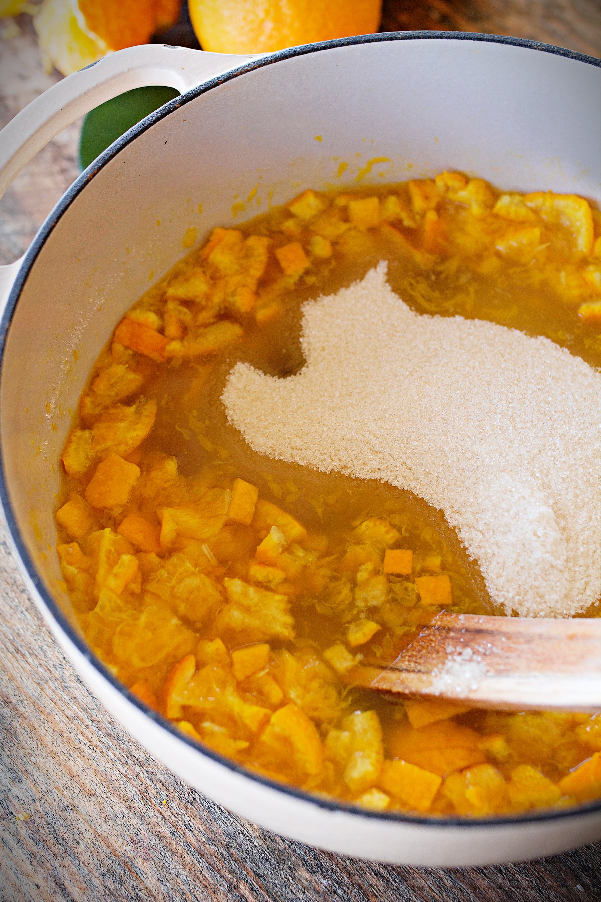 Sugar being added to diced oranges in stockpot.
