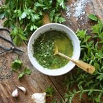 Chimichurri sauce in a white bowl on a wooden counter.