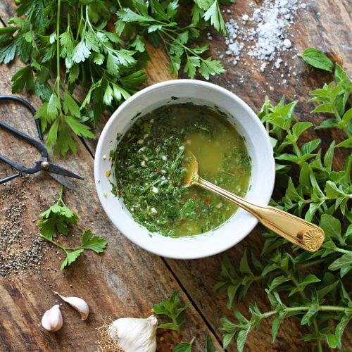 Chimichurri sauce in a white bowl on a wooden counter.