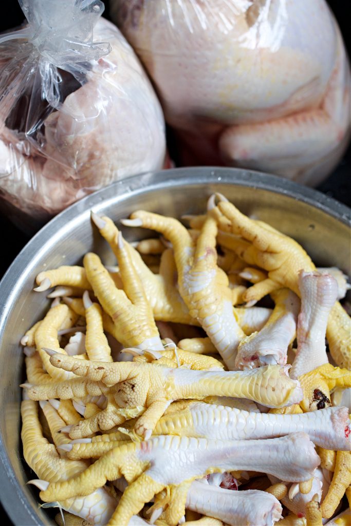 bowl of chicken feet after butchering and 2 whole packaged birds.