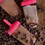 fudge popsicles laying in chocolate chips on a counter with sprinkles everywhere.