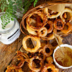 Onion Rings in basket on counter next to honey mustard dipping sauce.