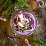 purple onions in a pint jar on counter with other herbs.