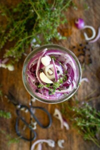 purple onions in a pint jar on counter with other herbs.