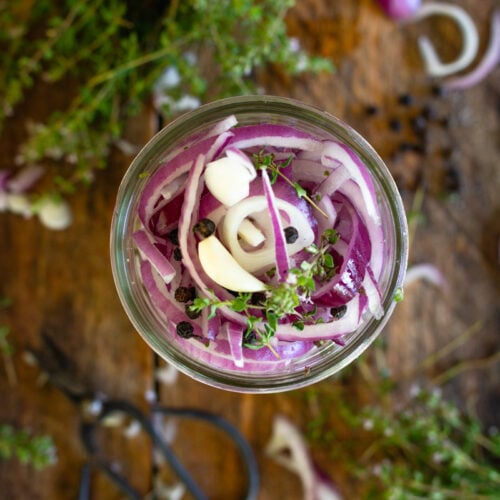purple onions in a pint jar on counter with other herbs.