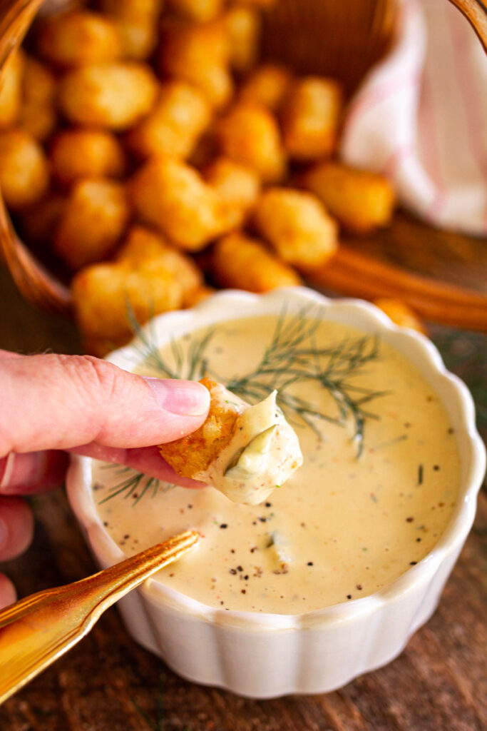 tater tots being dipped into tartar sauce.