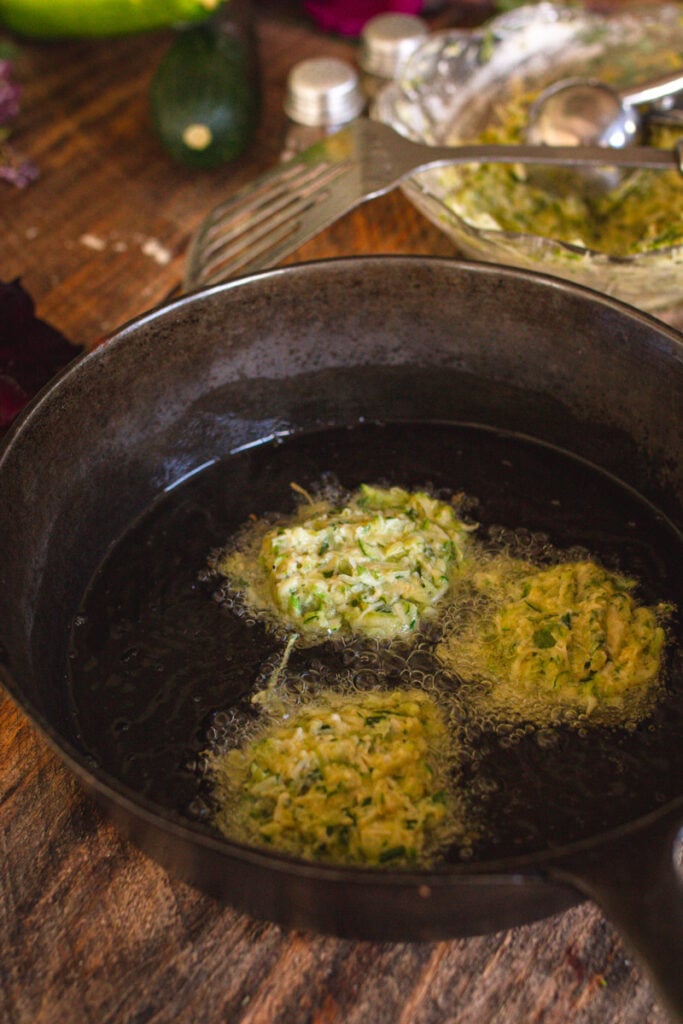 Zucchini fritters cooking in oil in cast iron pan.
