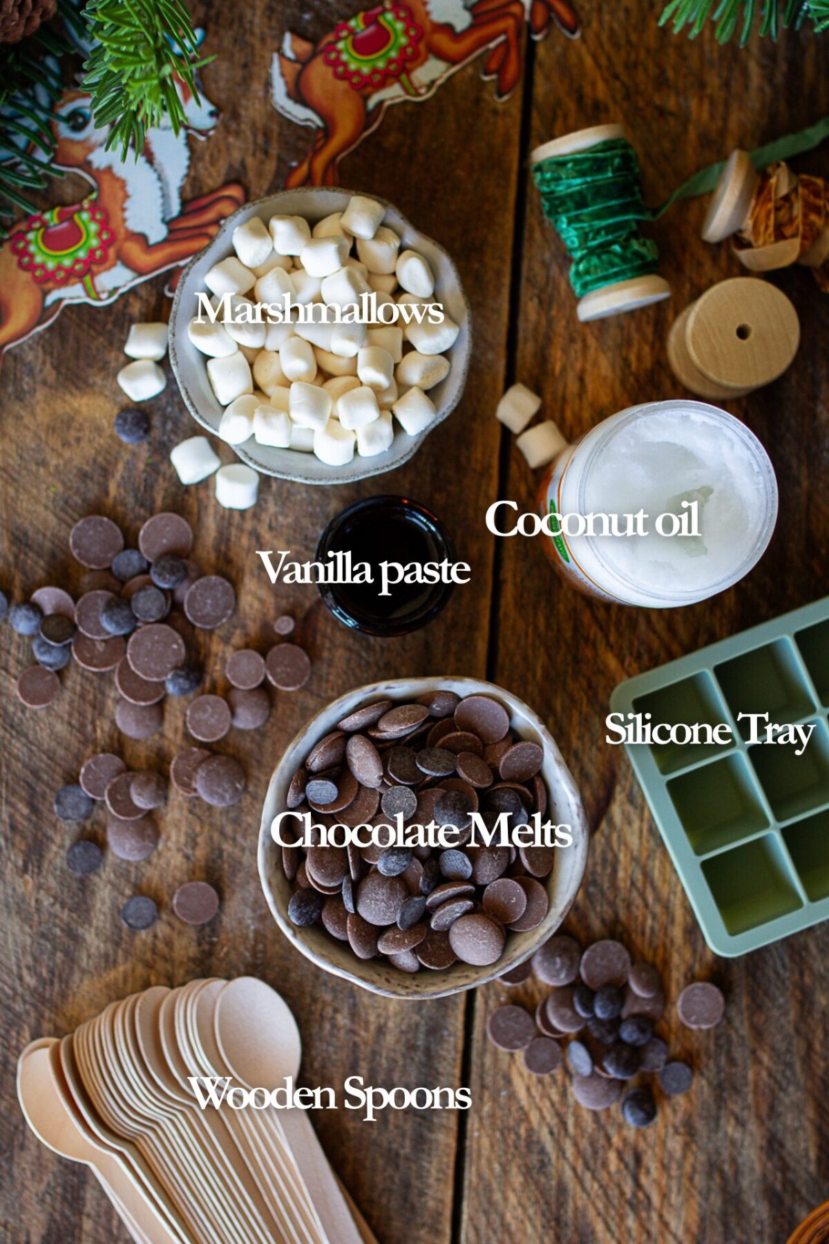 Ingredients for hot chocolate spoons: chocolate melts, coconut oil, vanilla paste, silicone tray, wooden spoons, marshmallows.