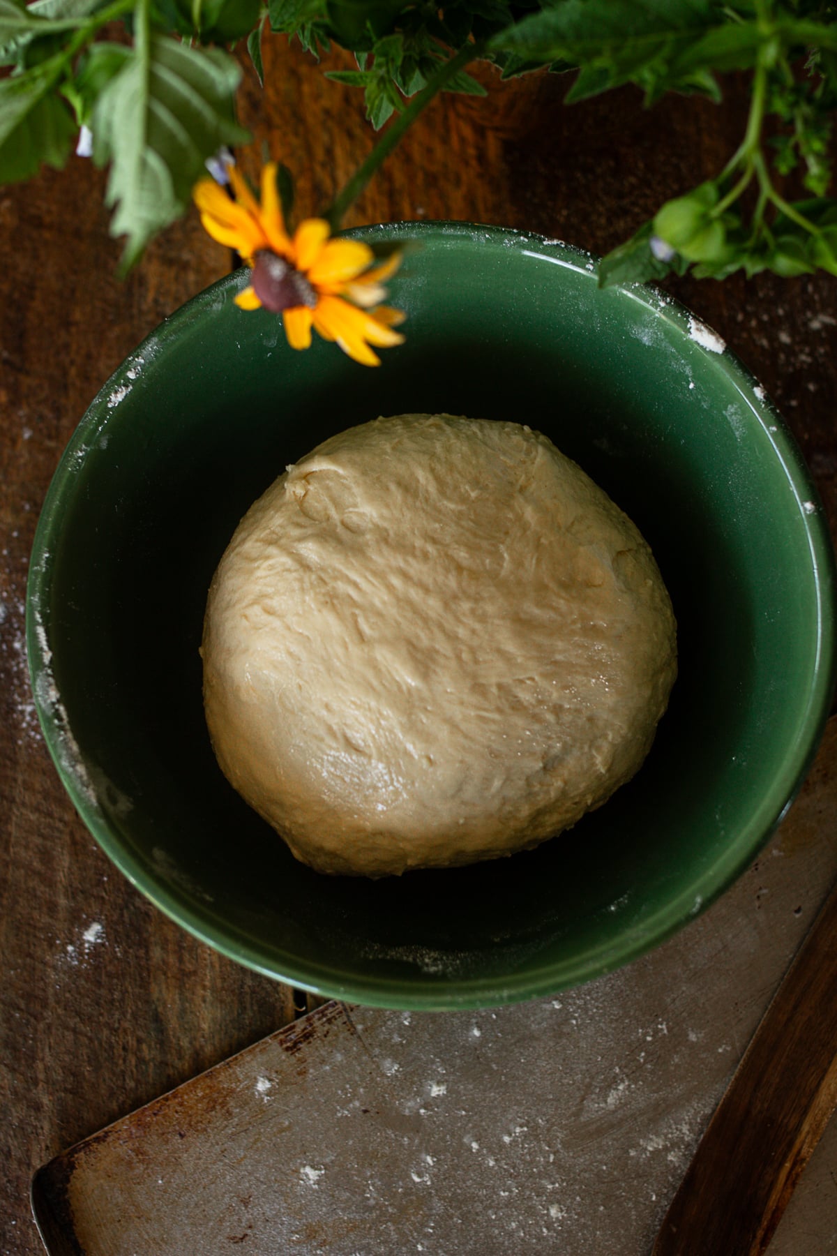 A top-down shot of a smooth ball of bread dough resting in a green ceramic bowl on a wooden table.