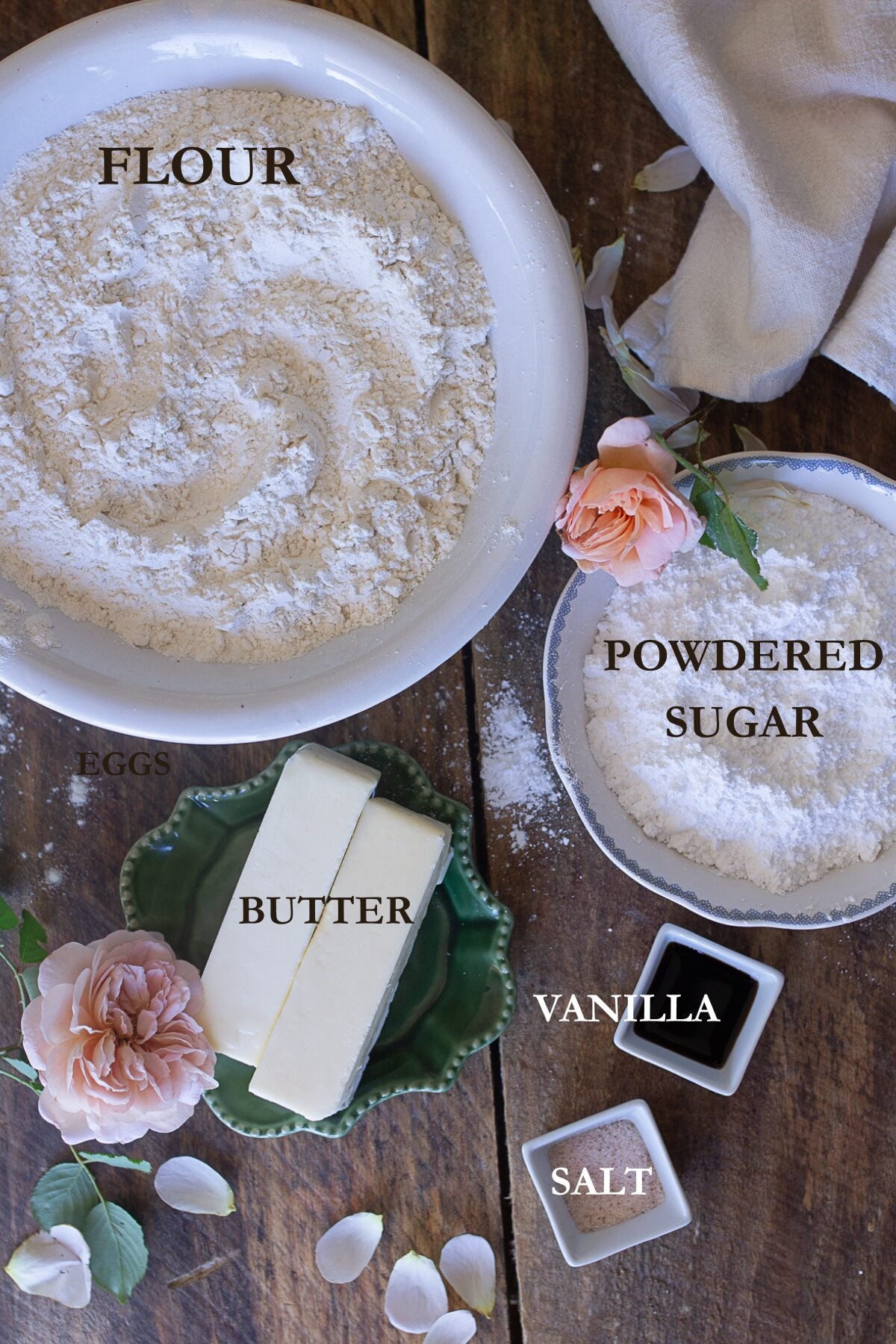 Butter, powdered sugar, flour, vanilla, and salt arranged on a rustic wooden table for homemade shortbread cookies.