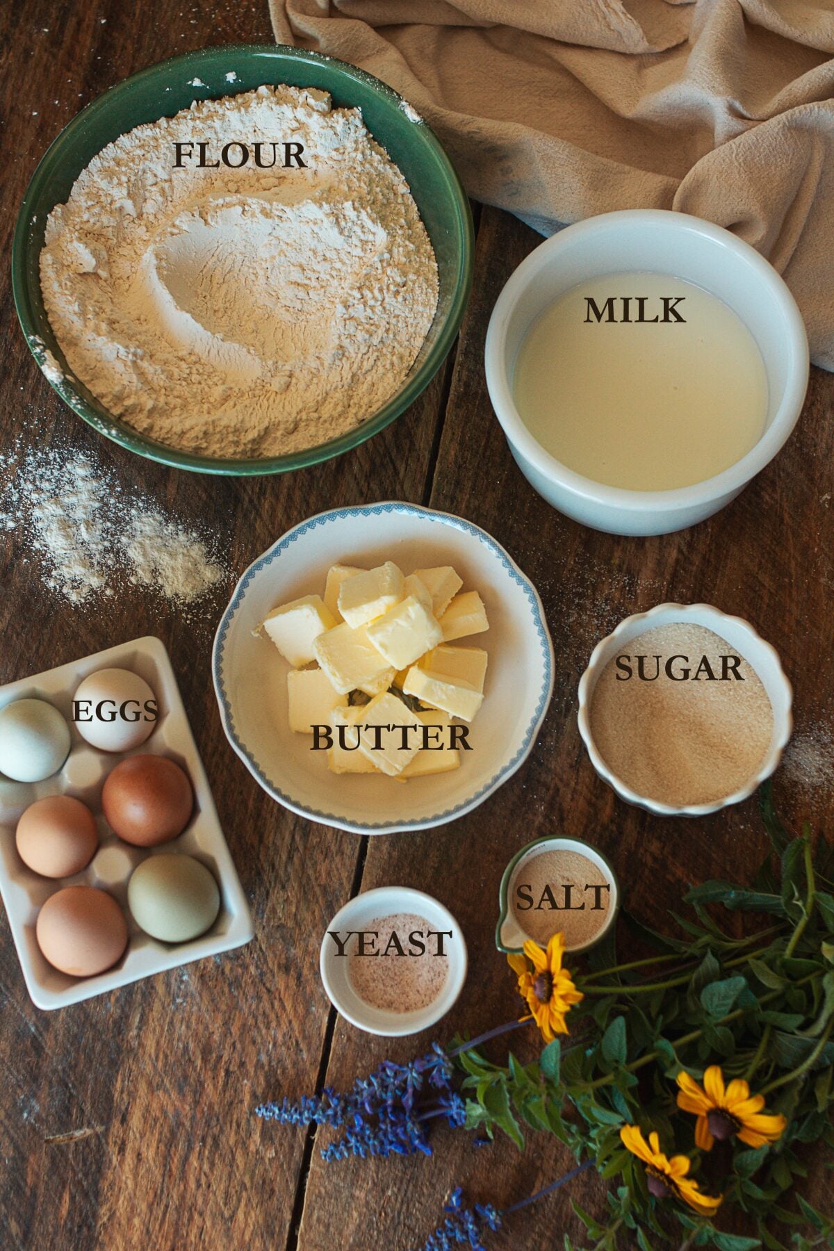 milk, flour, yeast, sugar, and salt come together to create rich homemade brioche buns.
Ingredients for homemade brioche buns including flour, milk, butter, eggs, sugar, yeast, and salt on a wooden table.