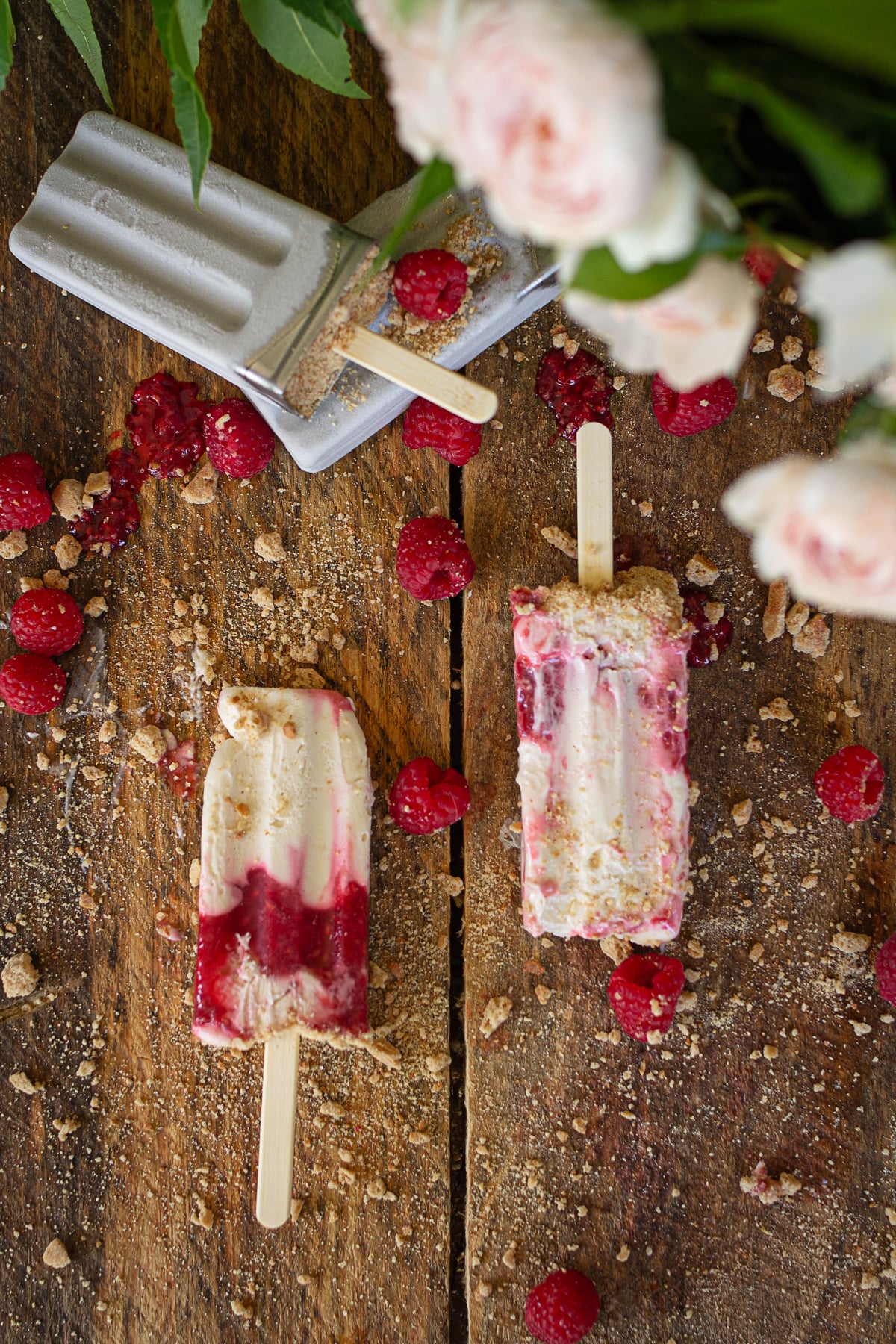 : An overhead view of two marbled raspberry cheesecake popsicles laying on a dark wood grain table.