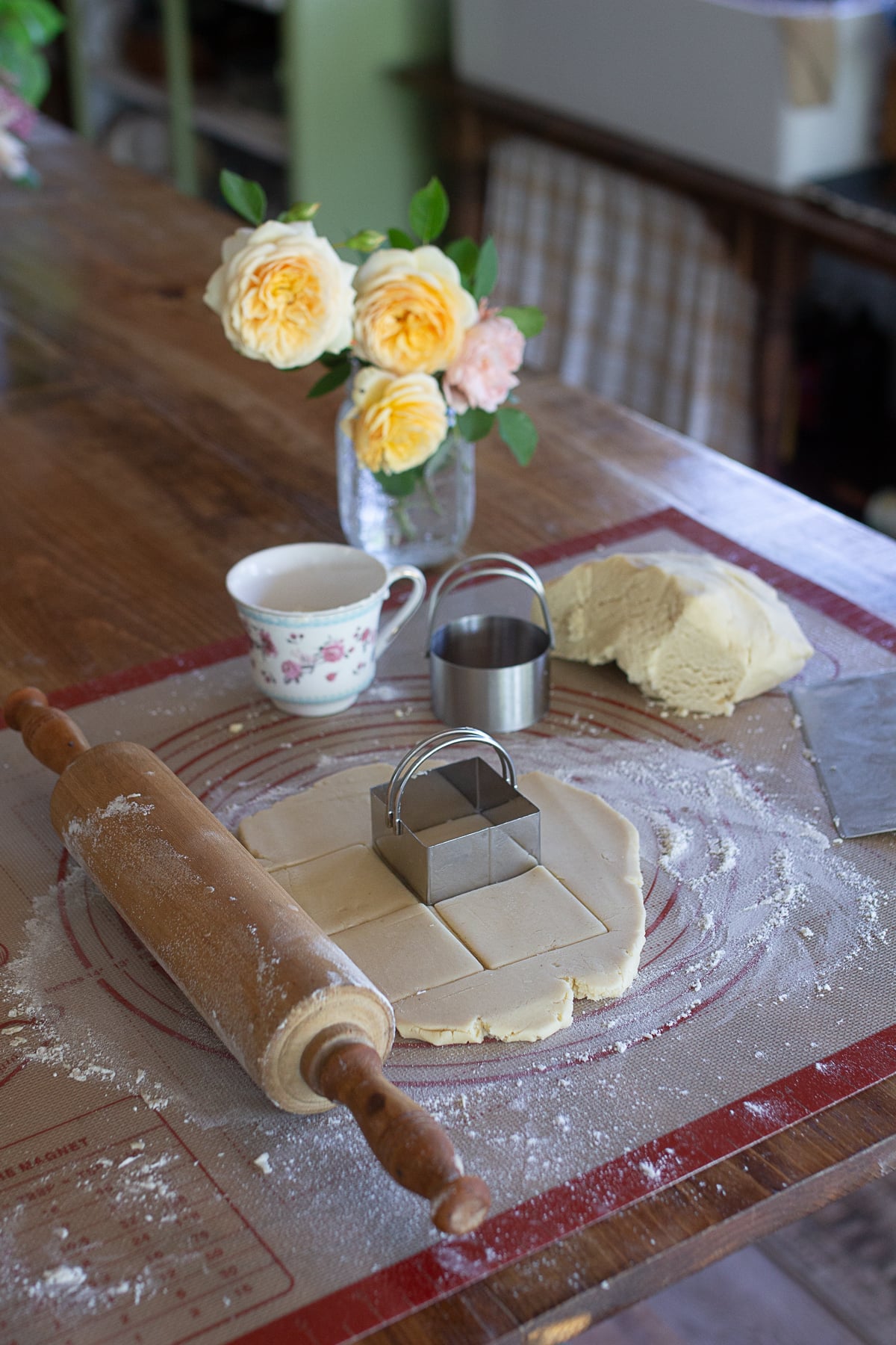 Shortbread cookie dough rolled out on a floured pastry mat with a rolling pin and square cookie cutter on a farmhouse table.