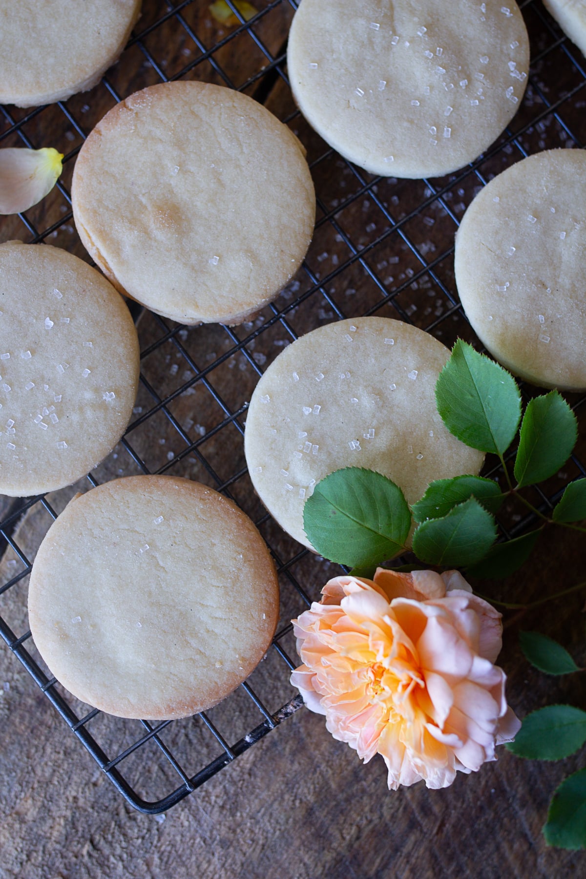 Round homemade shortbread cookies cooling on a wire rack with flower petals and coarse sugar.