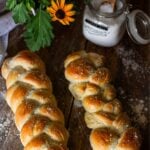 An overhead shot of two baked, golden-brown braided French bread loaves topped with coarse sea salt on a wooden counter.