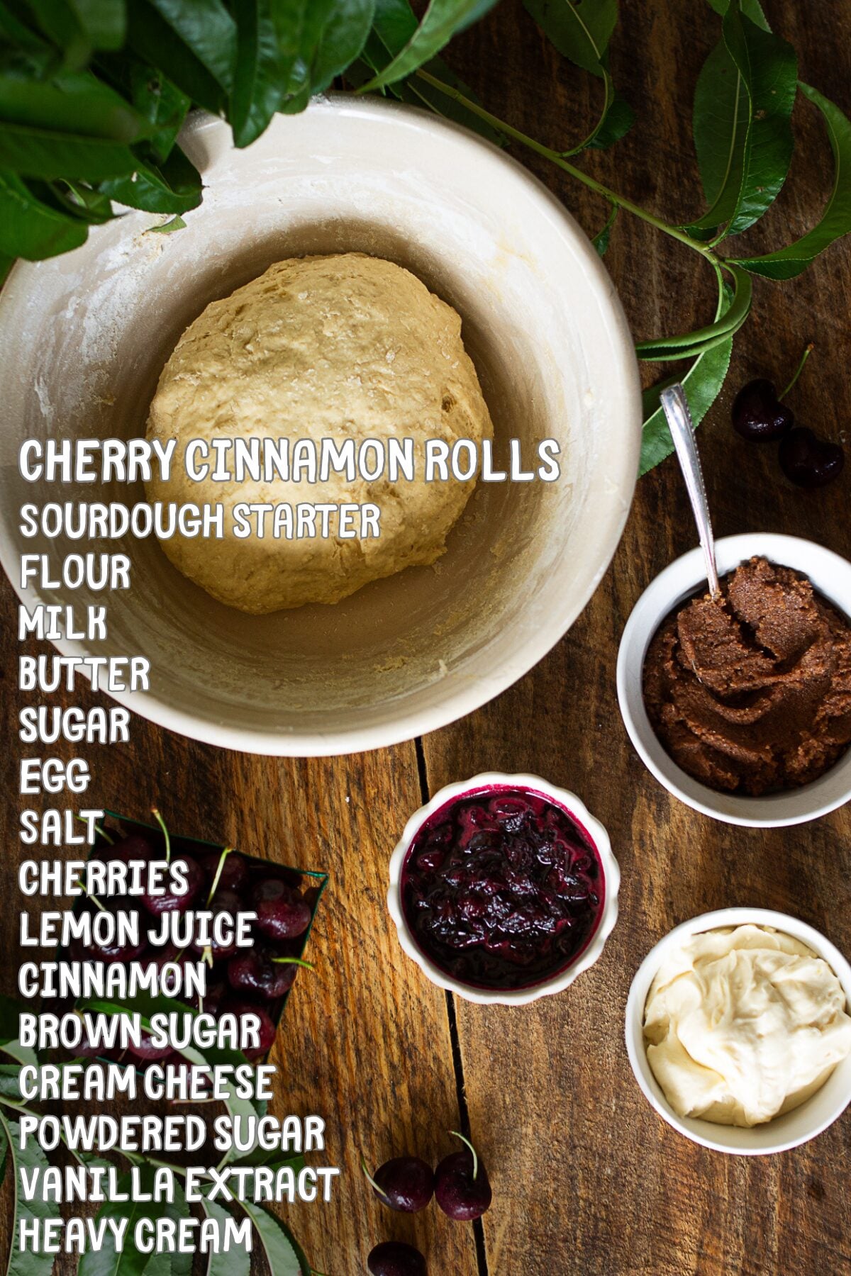 Overhead view of sourdough cherry cinnamon roll ingredients laid out on a rustic wood table with text overlay listing recipe ingredients