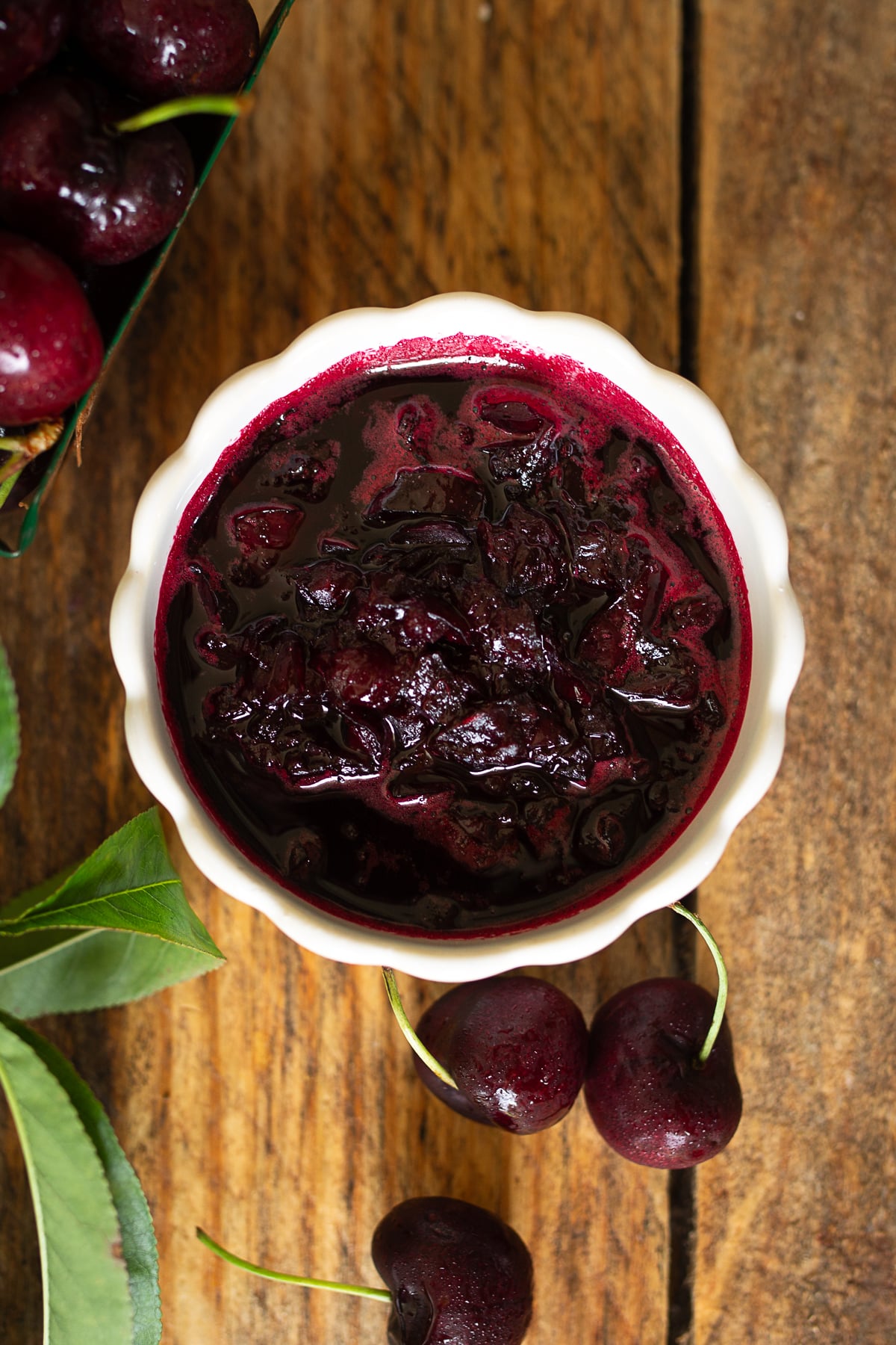 Small ceramic bowl filled with thick homemade sweet cherry sauce and fresh cherries on a wooden table