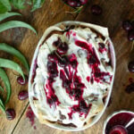 Overhead view of frosted sourdough cherry cinnamon rolls topped with cream cheese icing, fresh sweet cherries, and cherry sauce drizzle