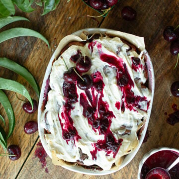 Overhead view of frosted sourdough cherry cinnamon rolls topped with cream cheese icing, fresh sweet cherries, and cherry sauce drizzle