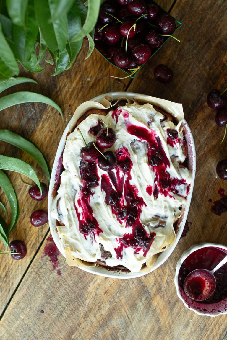 Overhead view of frosted sourdough cherry cinnamon rolls topped with cream cheese icing, fresh sweet cherries, and cherry sauce drizzle