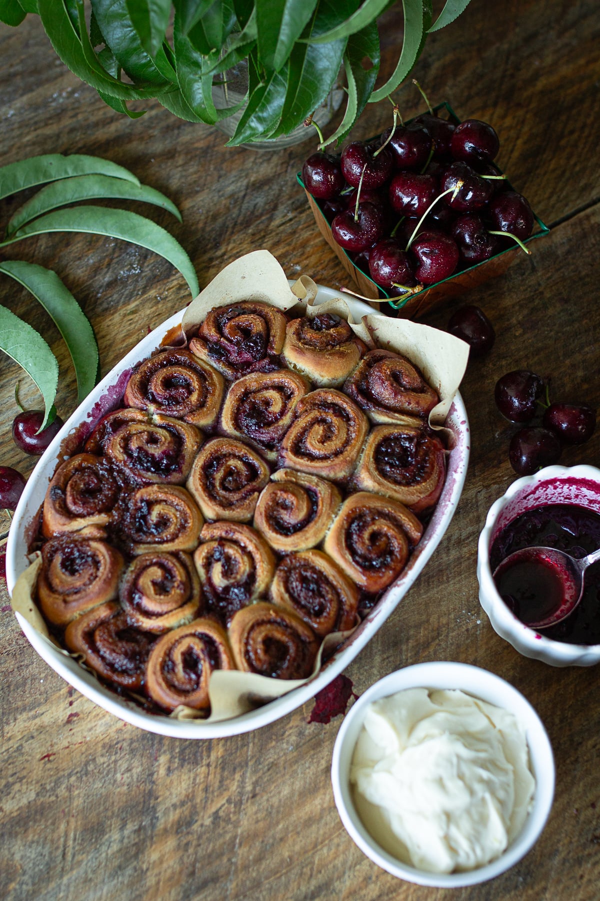 Baked sourdough cherry cinnamon rolls freshly out of the oven in a baking dish before frosting, served next to fresh sweet cherries