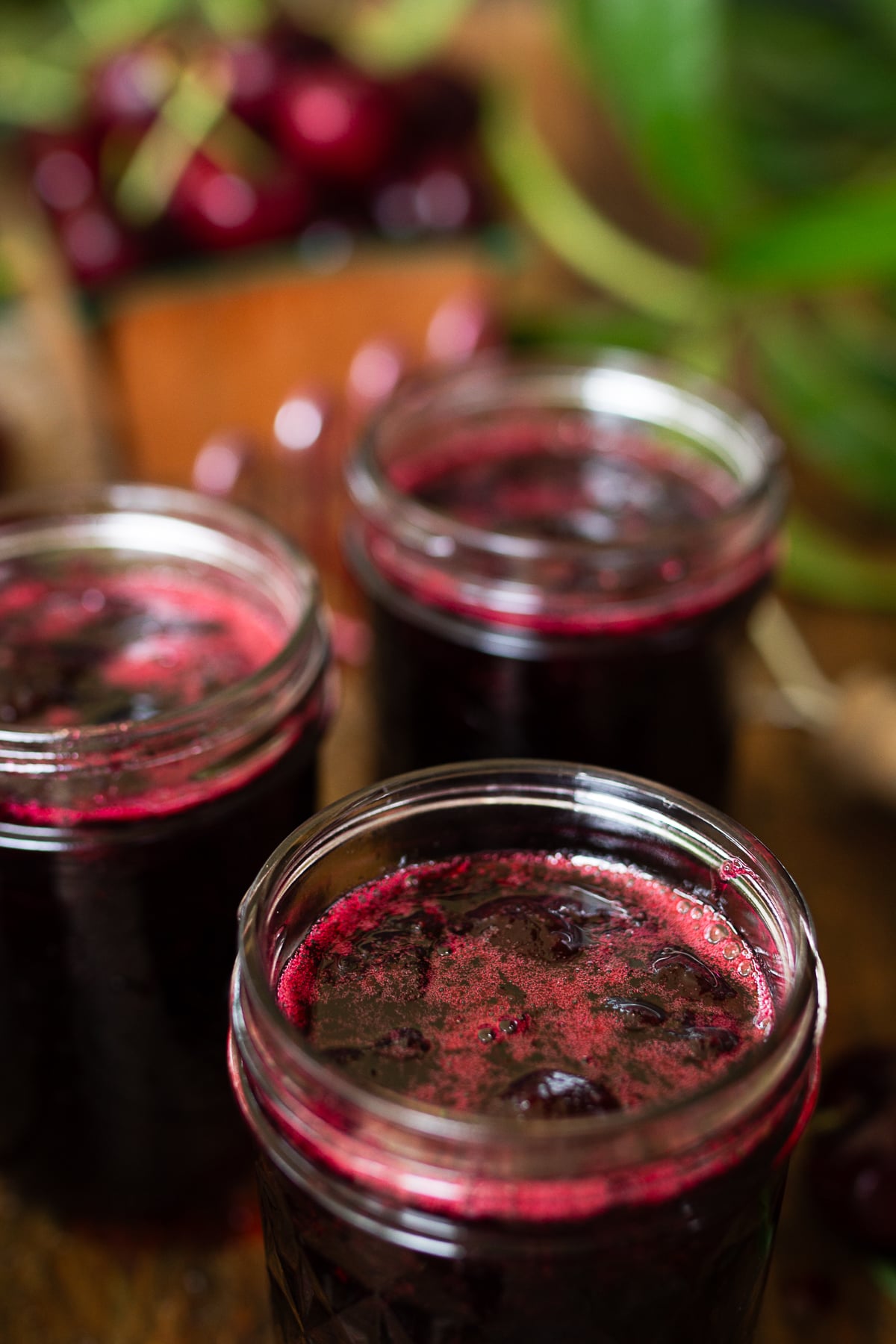 Close-up macro shot looking into the rims of clear glass mason jars filled with freshly made, vibrant red sweet cherry jam.