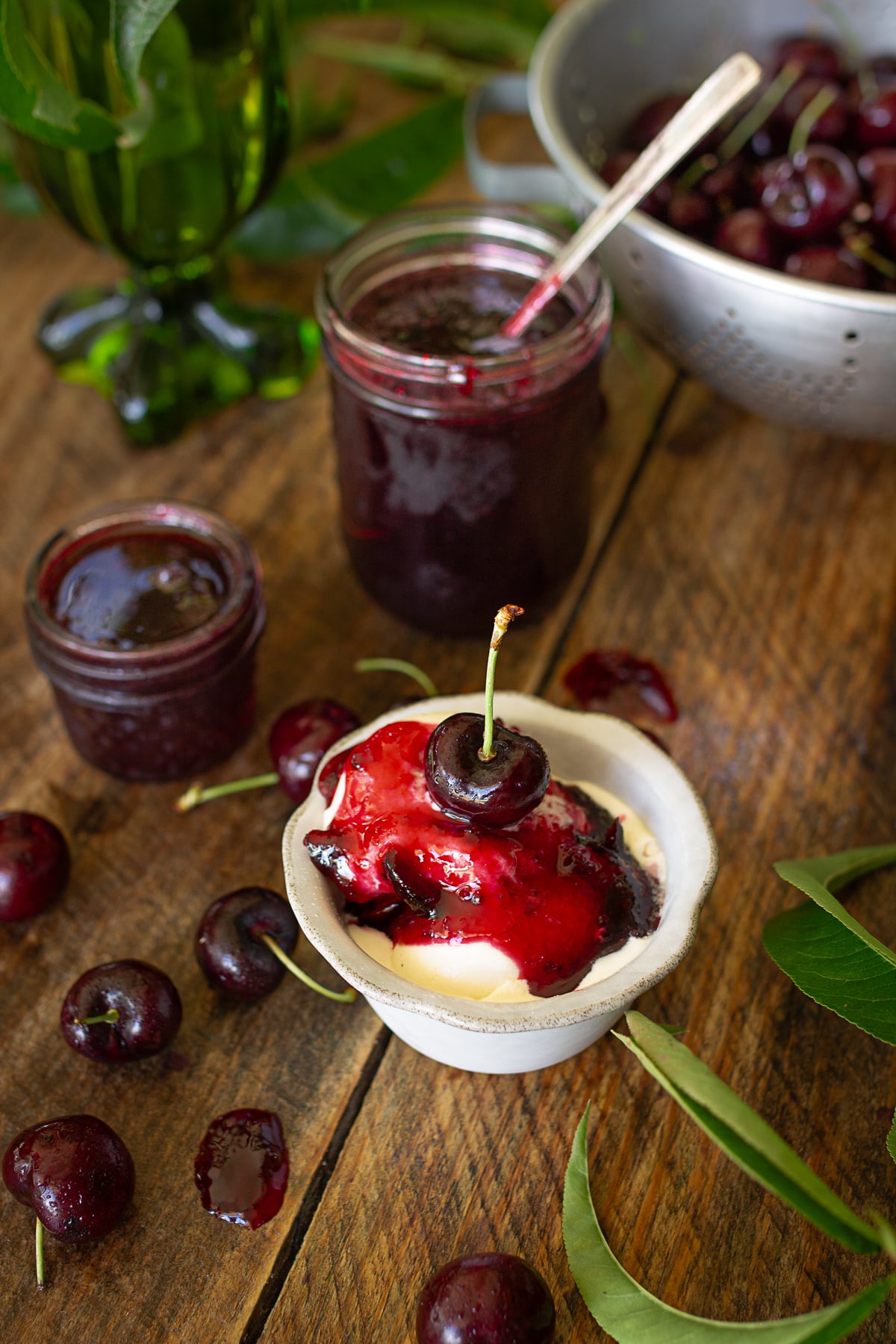 Close-up shot on a white bowl of vanilla ice cream with a pour of homemade sweet cherry jam, garnished with a single cherry on top.